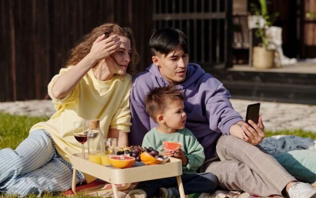 Famille assise dans l herbe qui consulte un smartphone, vérifier l affluence à Plopsaland De Panne