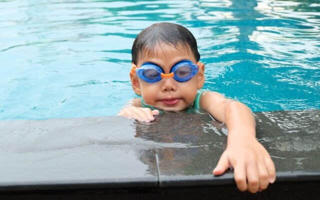 Jeune garçon avec des lunettes de natation au bord d'une piscine, l'entrée Aqualibi gratuite pour les enfants de moins de 1 m