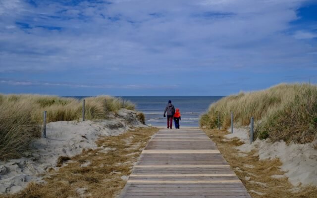 Parent et enfant sur un chemin en bois vers la plage dans les dunes, hébergement famille pas cher à La Panne