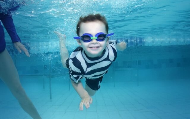 Garçon qui nage sous l'eau avec des lunettes dans une piscine, où le string de bain est interdit comme à Aqualibi